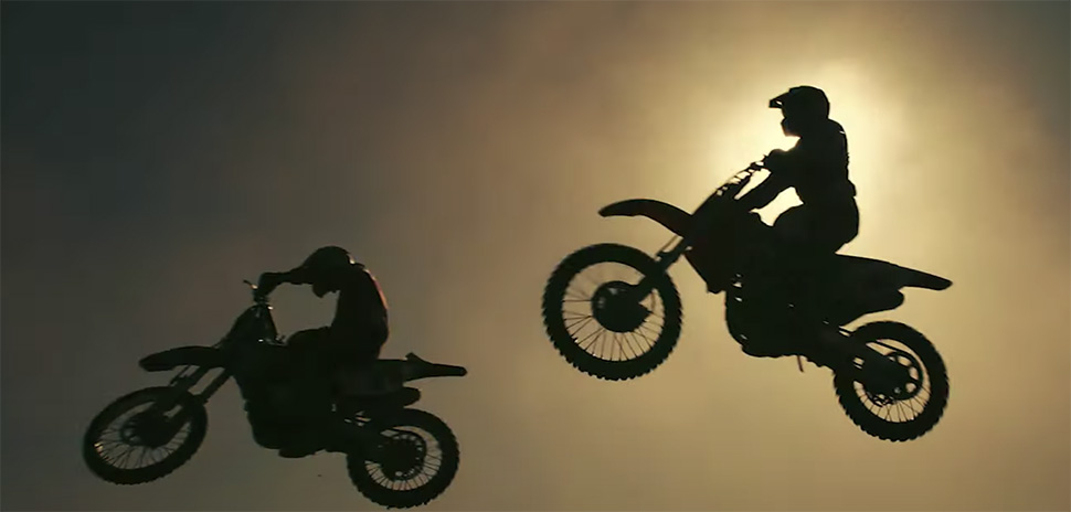 A view of two motorcyclists jumping in a sunset background