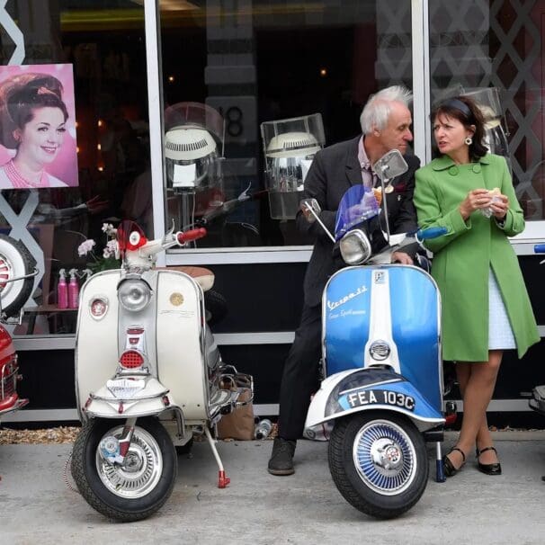 An old Italian couple next to a lineup of classic Vespa scoots. Media sourced from The Guardian.