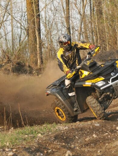 Rider in gear on yellow ATV tilting sideways in forest