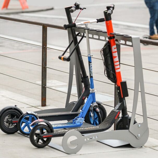 Three electric scooters locked onto a stand within inner-city