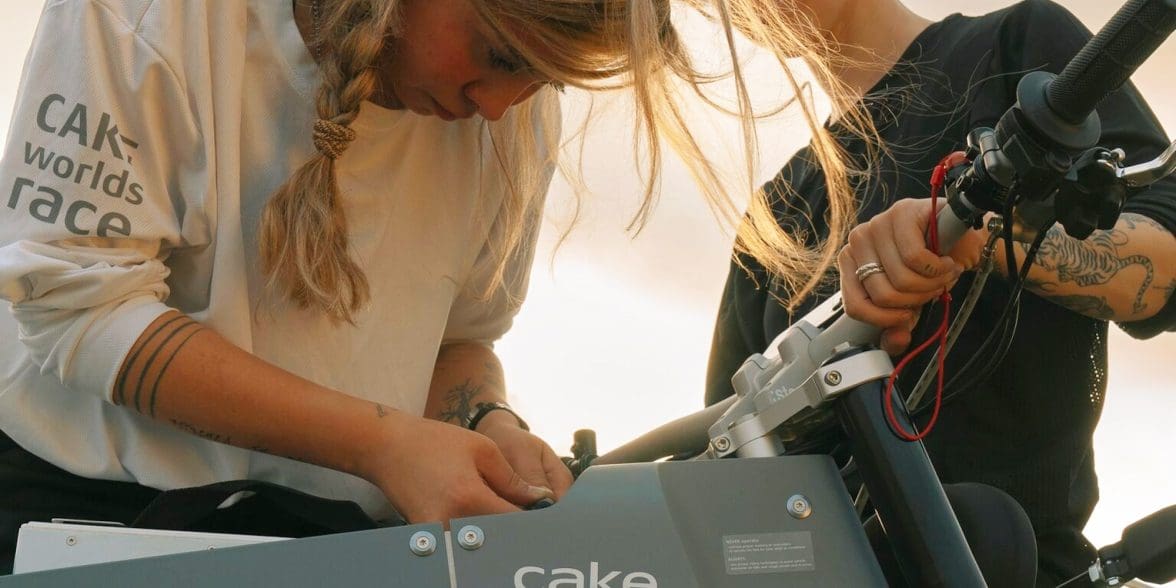 Two girls bending over an electric motorcycle.