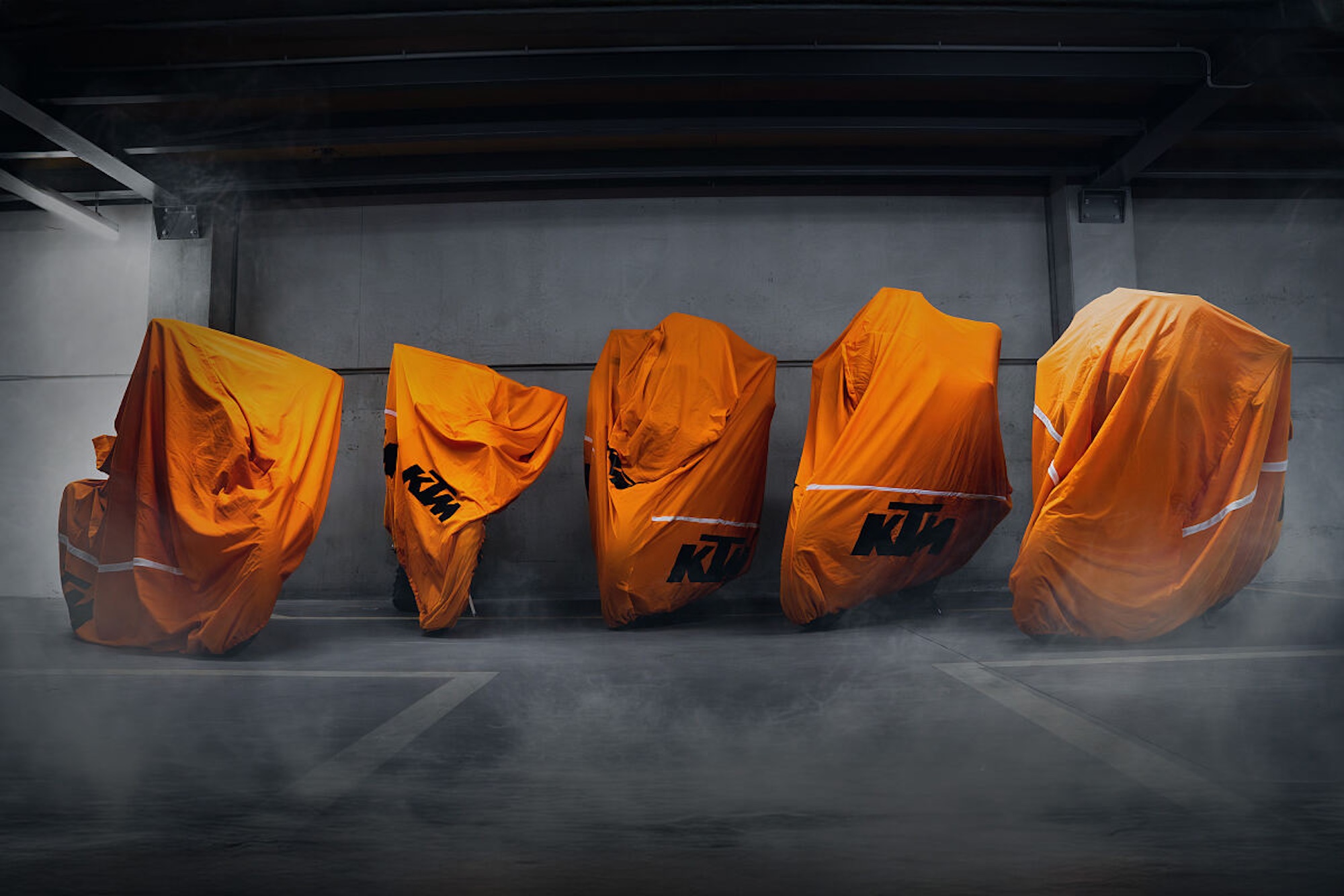 Five bikes under orange KTM covers.